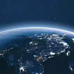 View of Earth from space at night showing illuminated cities and populated areas across Asia, with a star-filled sky in the background.