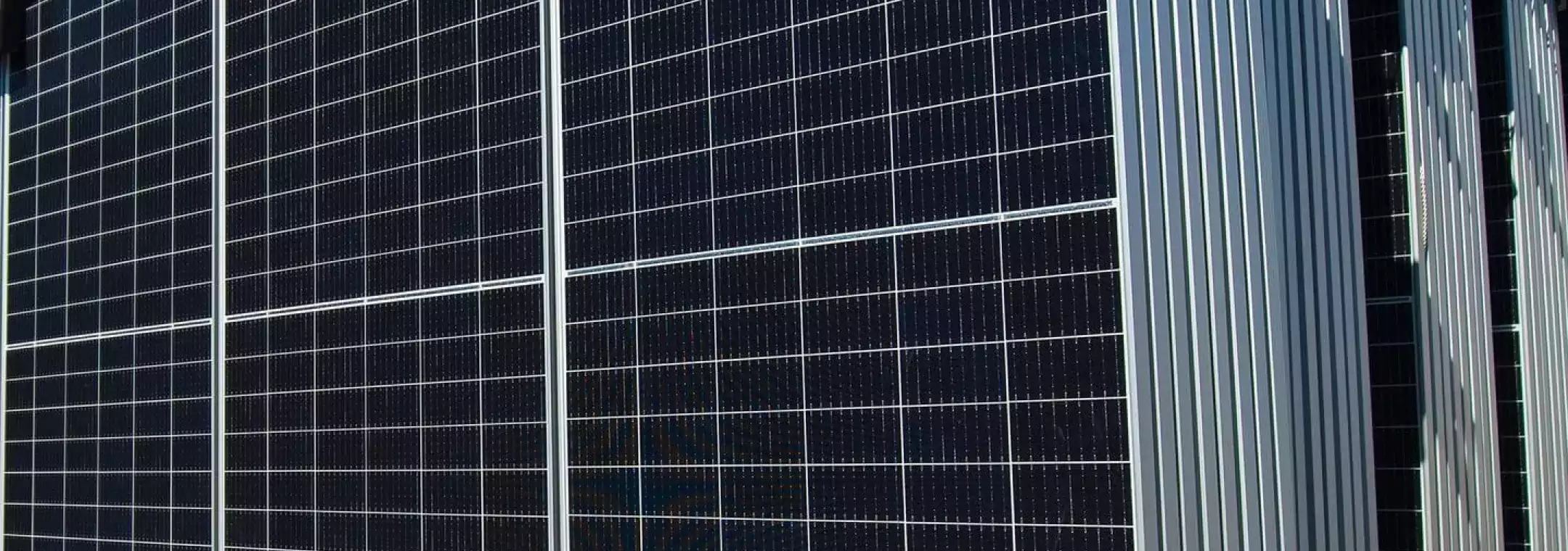 Close-up view of multiple large solar panels arranged in rows, reflecting sunlight against a clear blue sky.