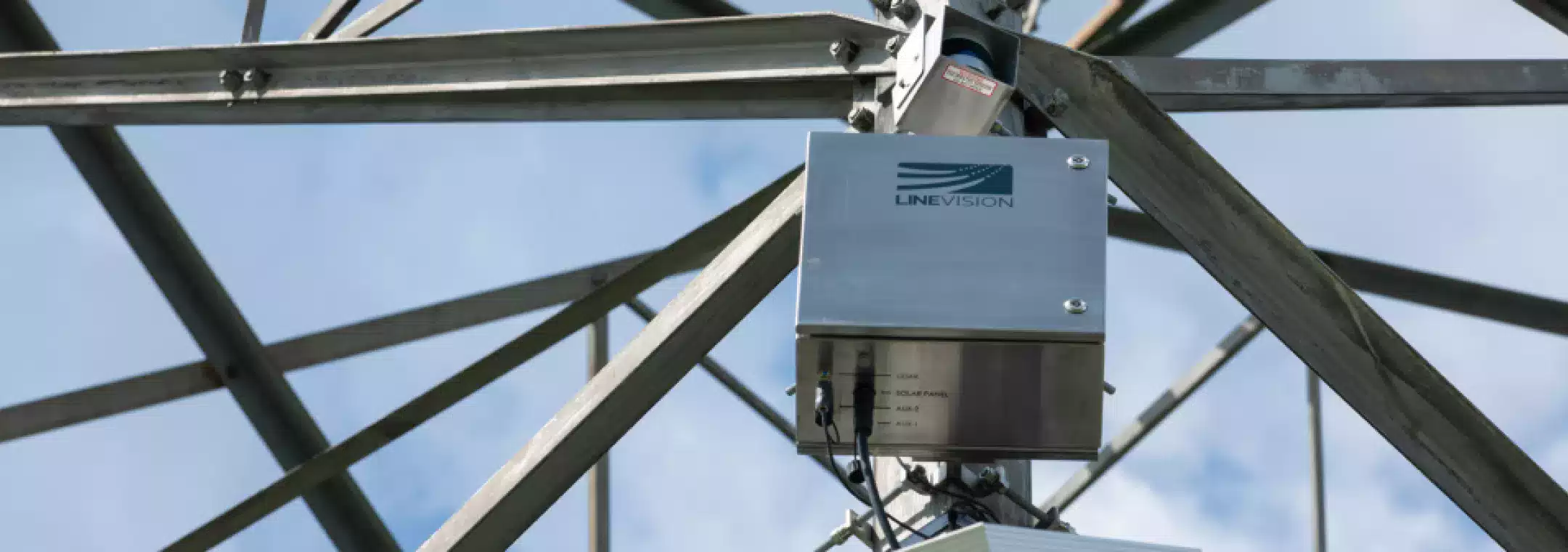 Close-up of a LineVision monitoring device installed on a metal utility tower structure against a blue sky background.