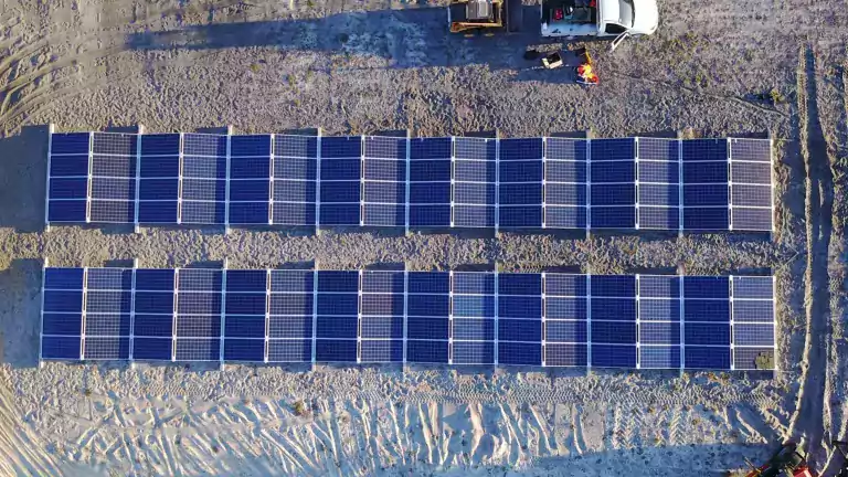 Aerial view of two rows of solar panels installed on sandy ground, with vehicles and workers nearby, illustrating a solar energy construction site.