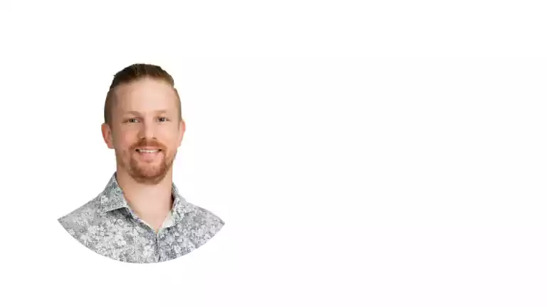 Smiling man with short light brown hair and beard wearing a patterned shirt, positioned on the left side of a white background.