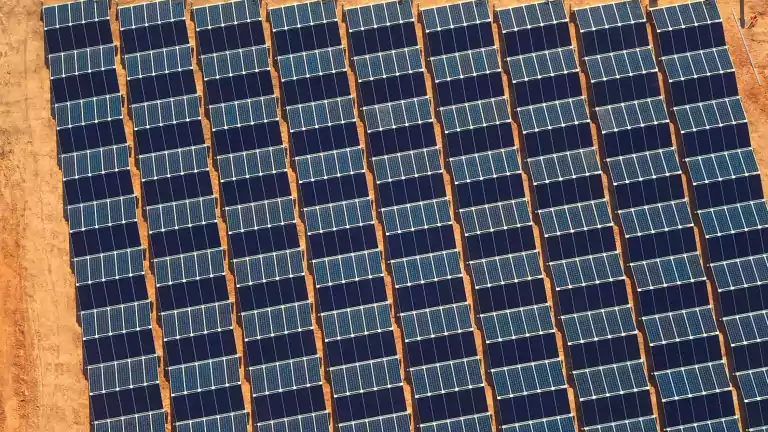 Aerial view of multiple rows of solar panels installed on a dry, sandy field, capturing sunlight for renewable energy production.
