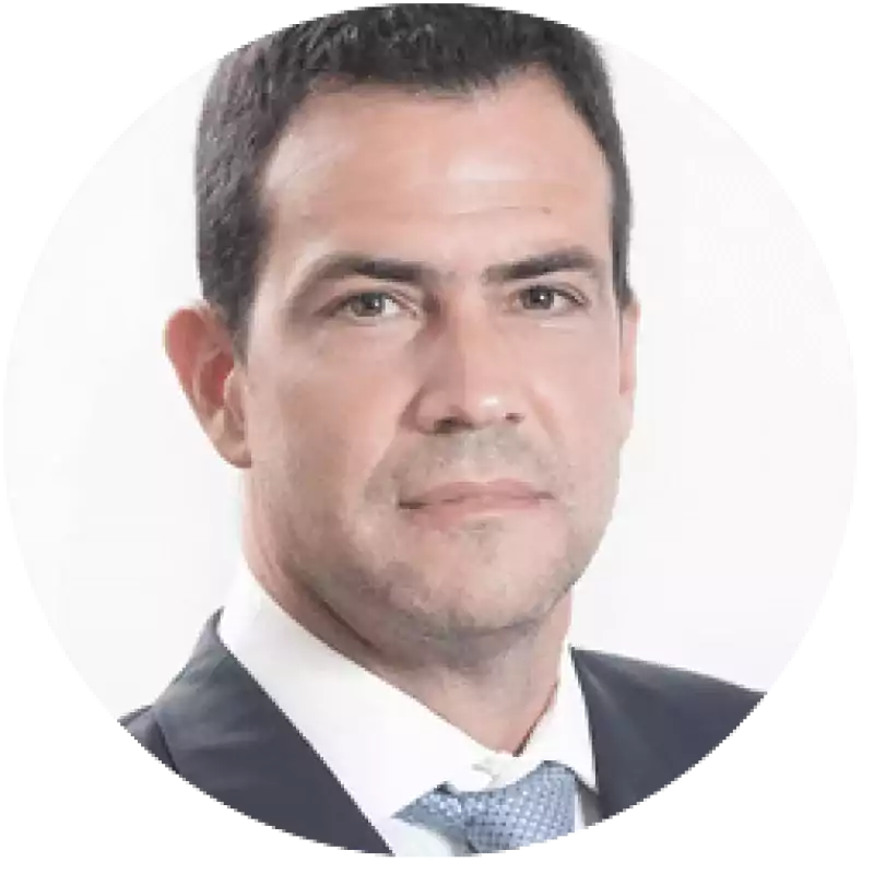 Portrait of a man with short dark hair wearing a dark suit, white shirt, and light blue tie, looking directly at the camera against a plain white background.