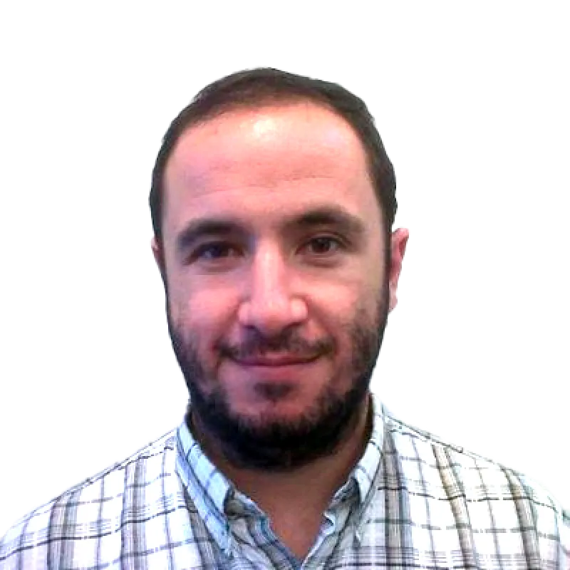 Un hombre con cabello oscuro corto y barba, vistiendo una camisa a cuadros, sonriendo a la cámara contra un fondo blanco liso.