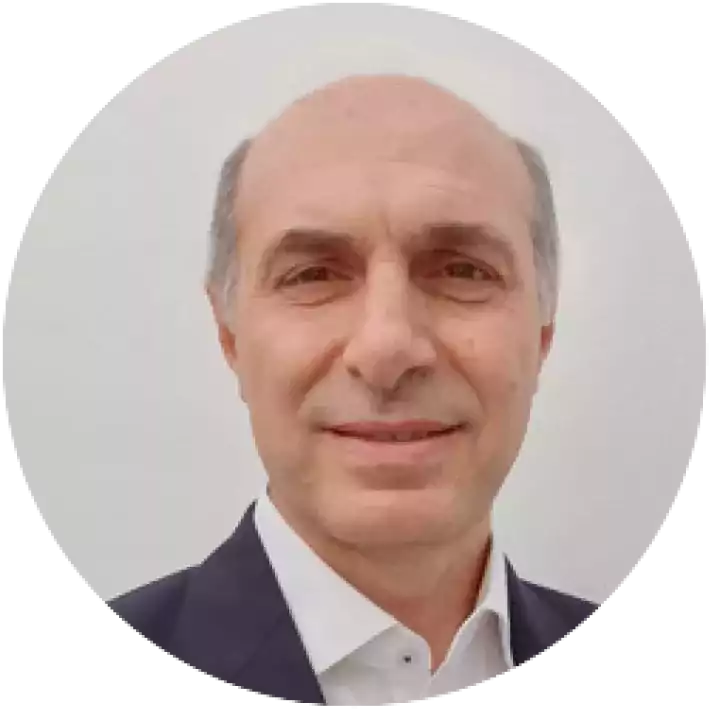 Portrait of a middle-aged man with short gray hair, wearing a dark suit jacket and white shirt, smiling slightly in front of a plain light background.
