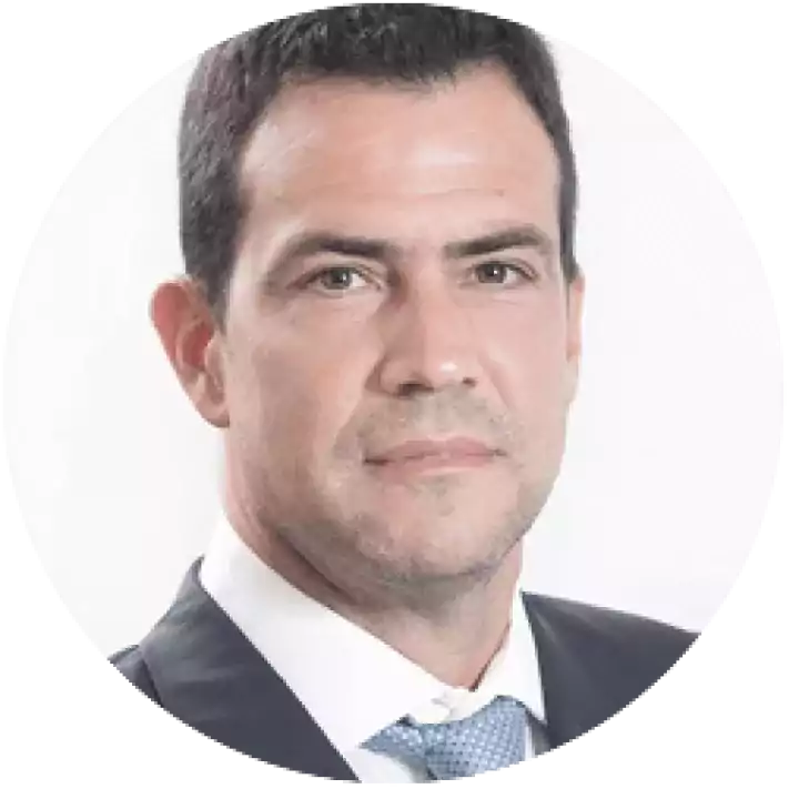 Portrait of a man with short dark hair wearing a dark suit, white shirt, and light blue tie, looking directly at the camera against a plain white background.