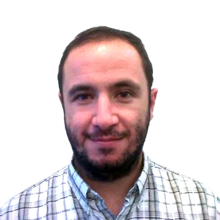 Un hombre con cabello oscuro corto y barba, vistiendo una camisa a cuadros, sonriendo a la cámara contra un fondo blanco liso.